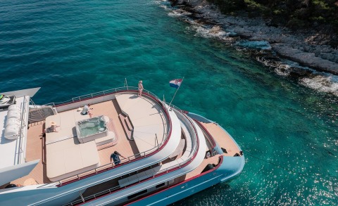 Ohana luxury yacht at anchor near rocky coastline, turquoise sea and deck lounge area