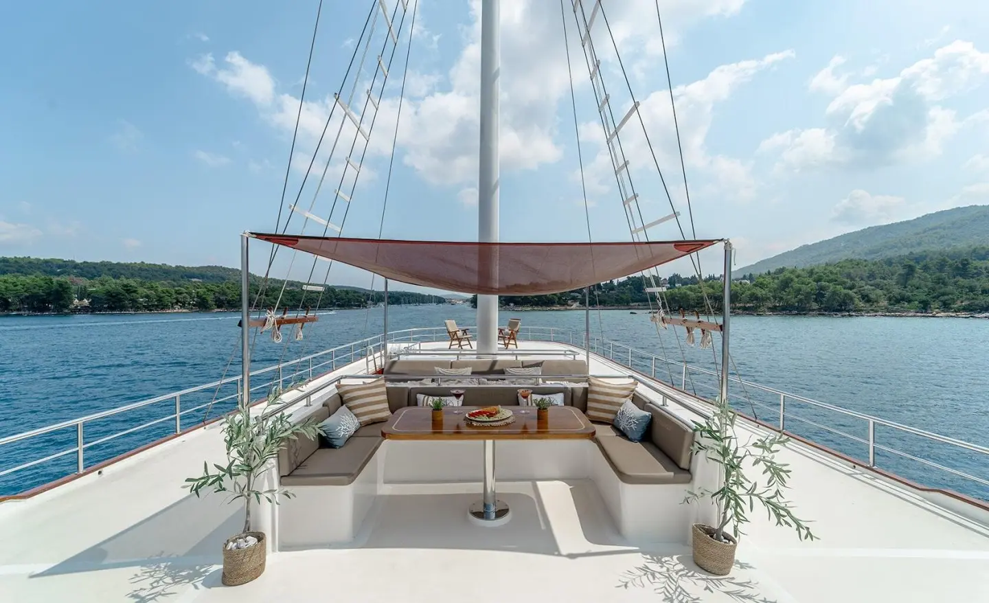 Cesarica sailing yacht bow seating area with table and shade sail on calm blue water