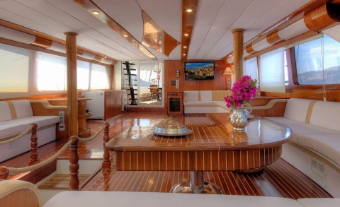 Angelo II interior: luxurious salon with polished wood, white seating, central table, flowers, and large windows