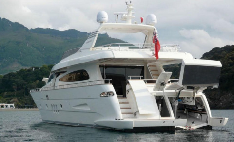 White motor yacht Miraval anchored in calm water with aft deck open and coastal hills in background