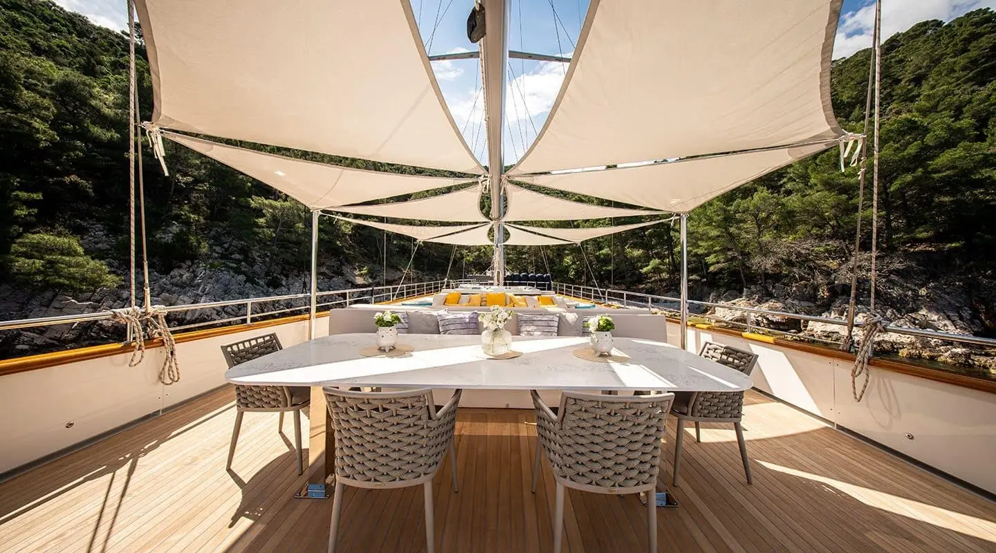 Dalmatino yacht deck dining area with wooden table and wicker chairs under a canopy
