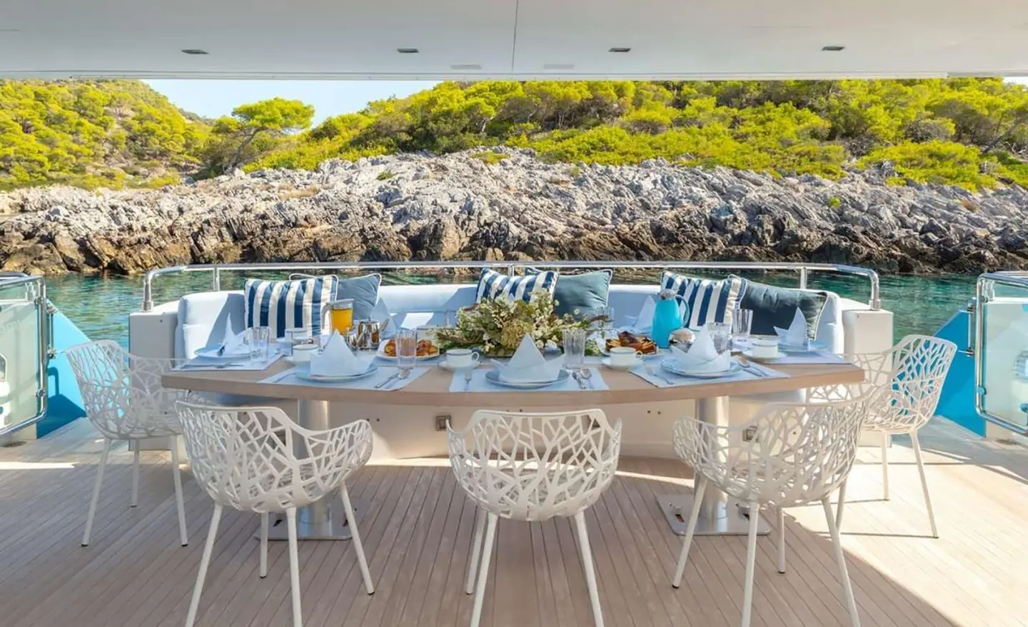 Sea Wolf yacht dining on deck with rocky coastline and greenery in background