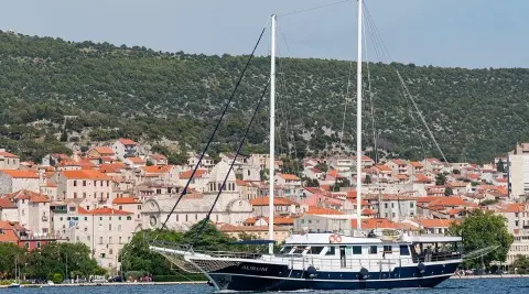 Auriun? No, image shows a luxurious sailing yacht named Aurum docked by a coastal town with red-tiled roofs at sunset