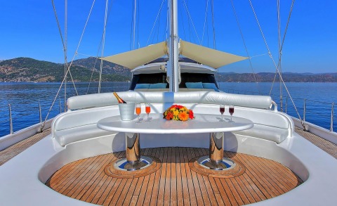 White seating area with a round table on the deck, floral centerpiece and champagne glasses, blue sea and hills in the background