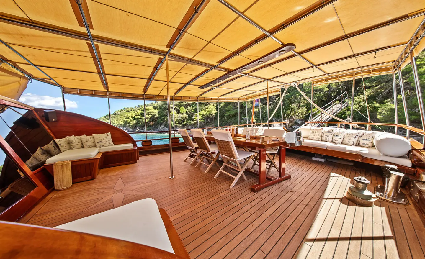 Eleganza yacht deck with wooden planks, shaded seating, and dining table under canvas at sunset