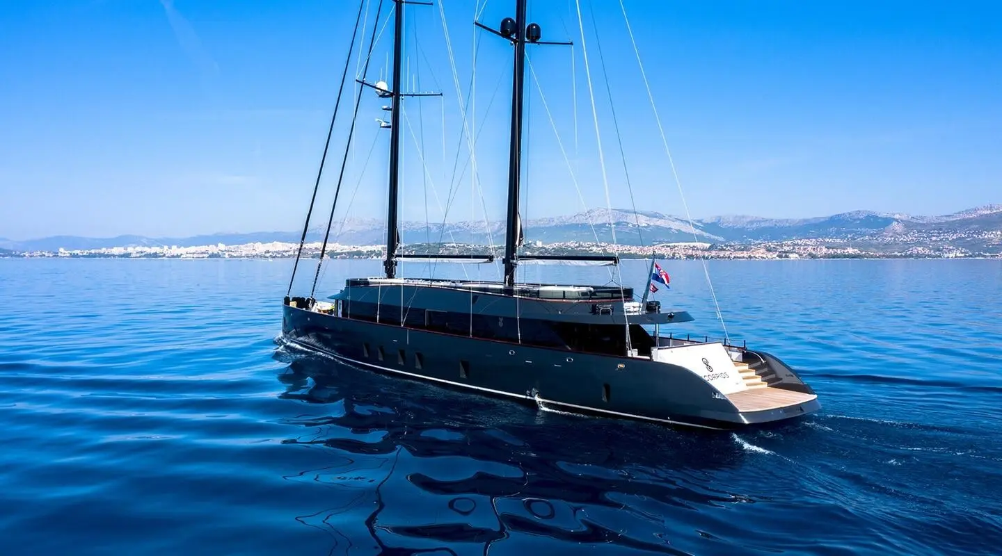 Two-masted motor yacht cruising on blue sea with distant coastline