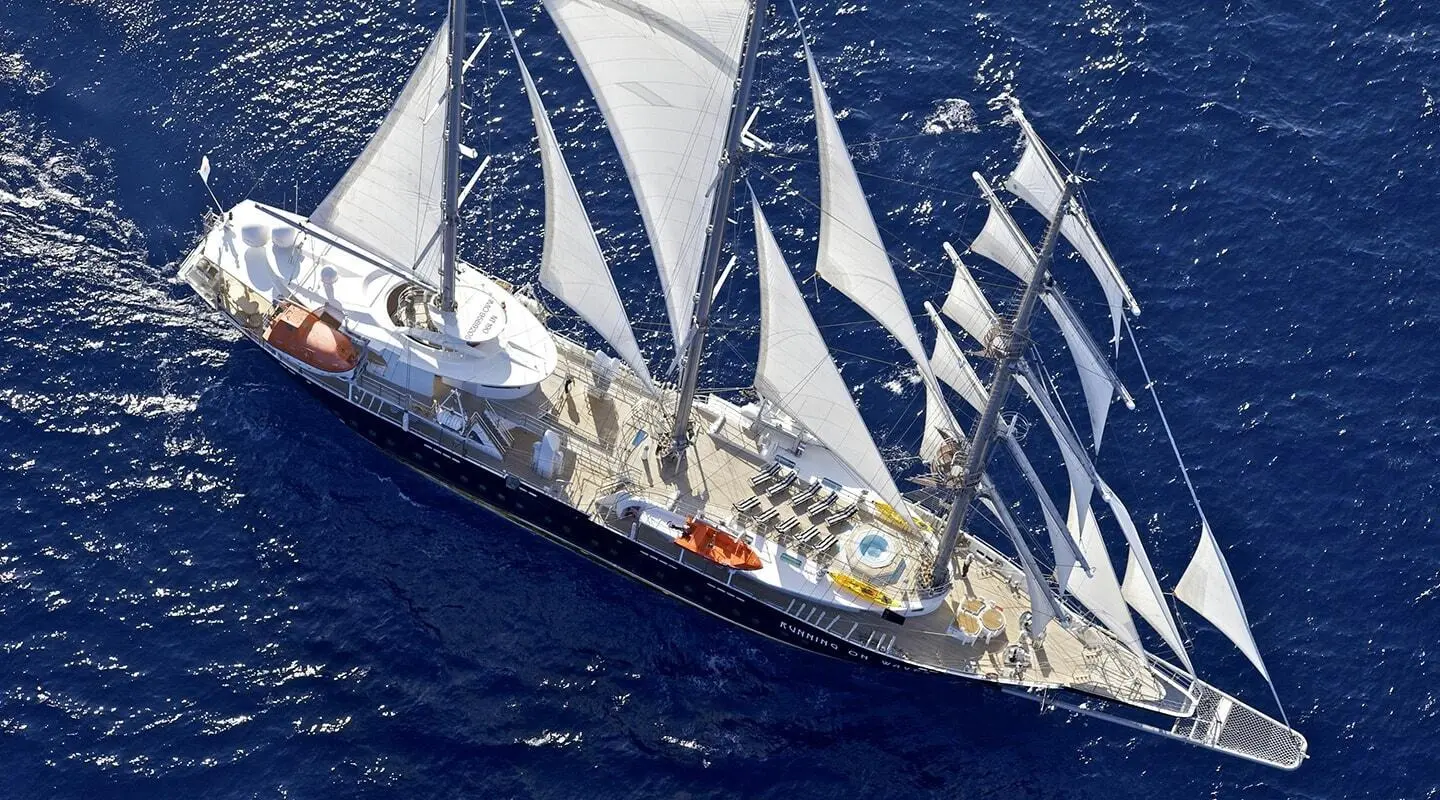 Yacht named Running on Waves sails at sunset on blue sea with multiple masts