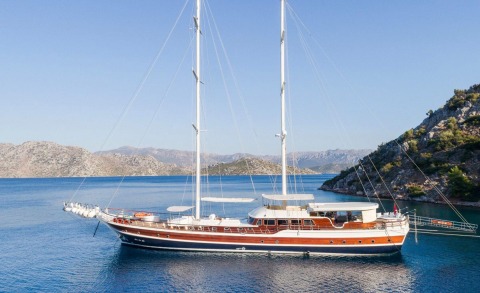 Halcon Del Mar sailing yacht anchored in calm blue seas with rugged coastline in the background