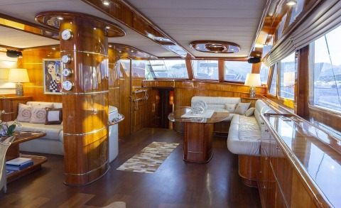 Luxurious yacht interior with wooden cabinets and seating, white sofa on the right and windows with sea view