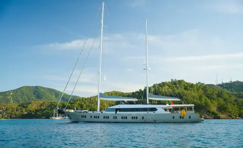 Two-masted yacht anchored by the shore with green hills and blue sky in the background