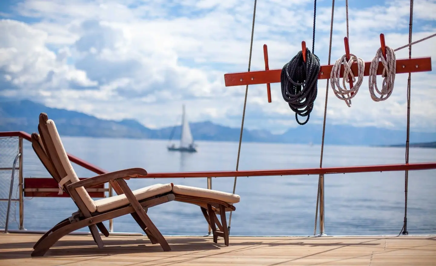 Romanca yacht on calm sea with wooden deck and lounge chairs at sunset