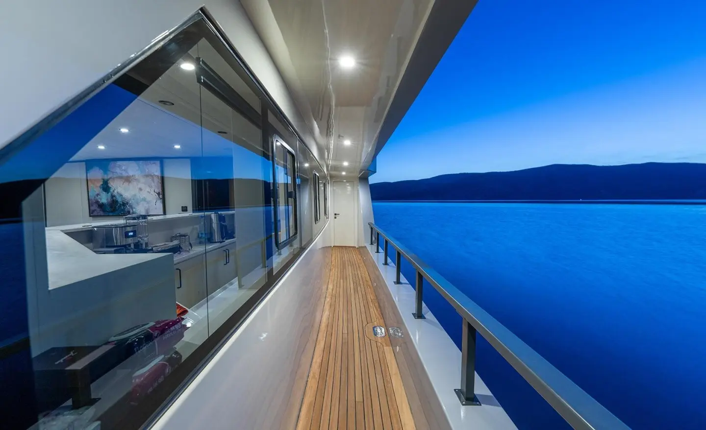 Sunlit yacht deck with polished wood, glass railing, and blue sea view