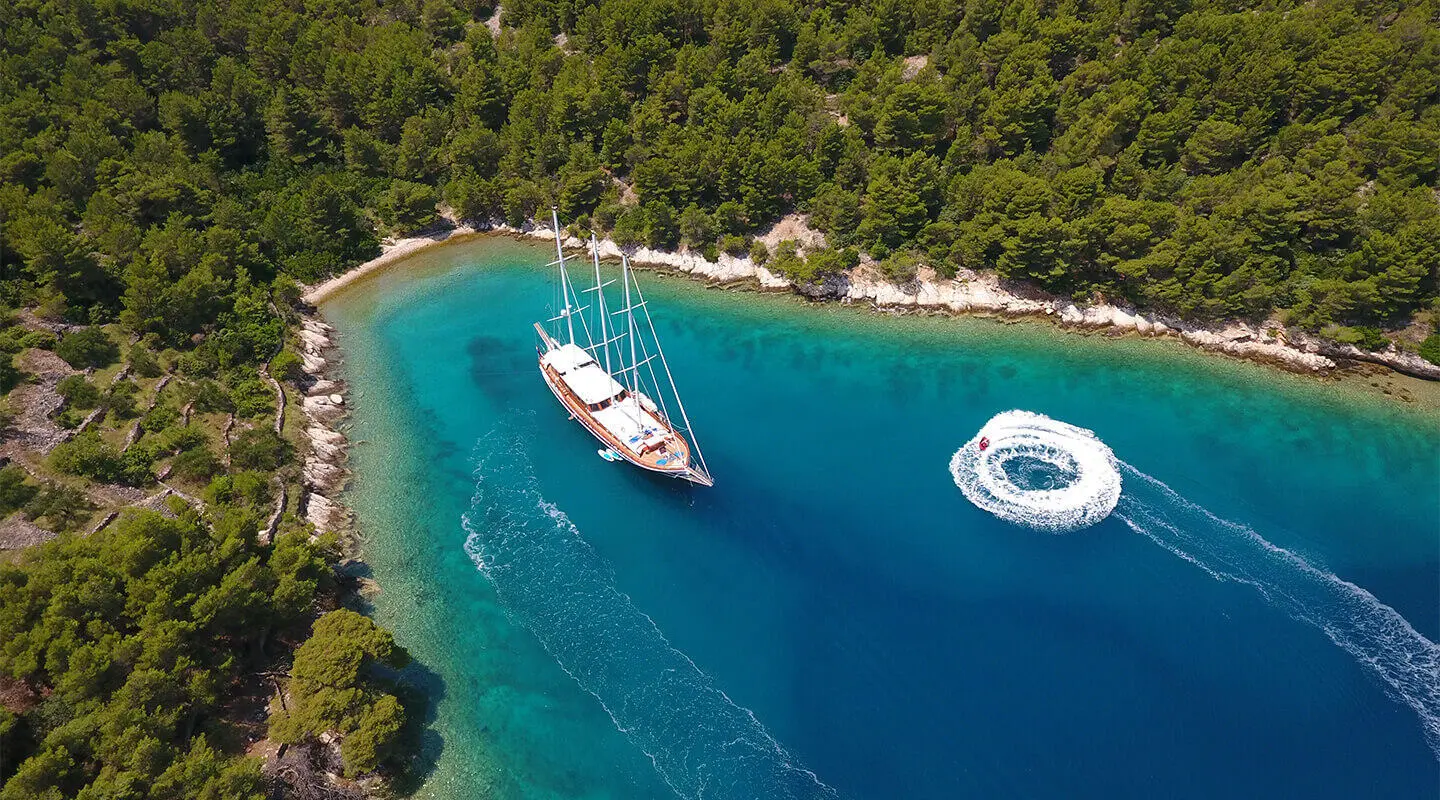 Dolce Vita yacht anchored near a rocky coastline with a sailboat nearby at sunset