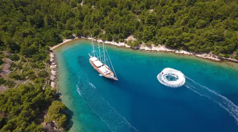 Dolce Vita yacht anchored near a rocky coastline with a sailboat nearby at sunset