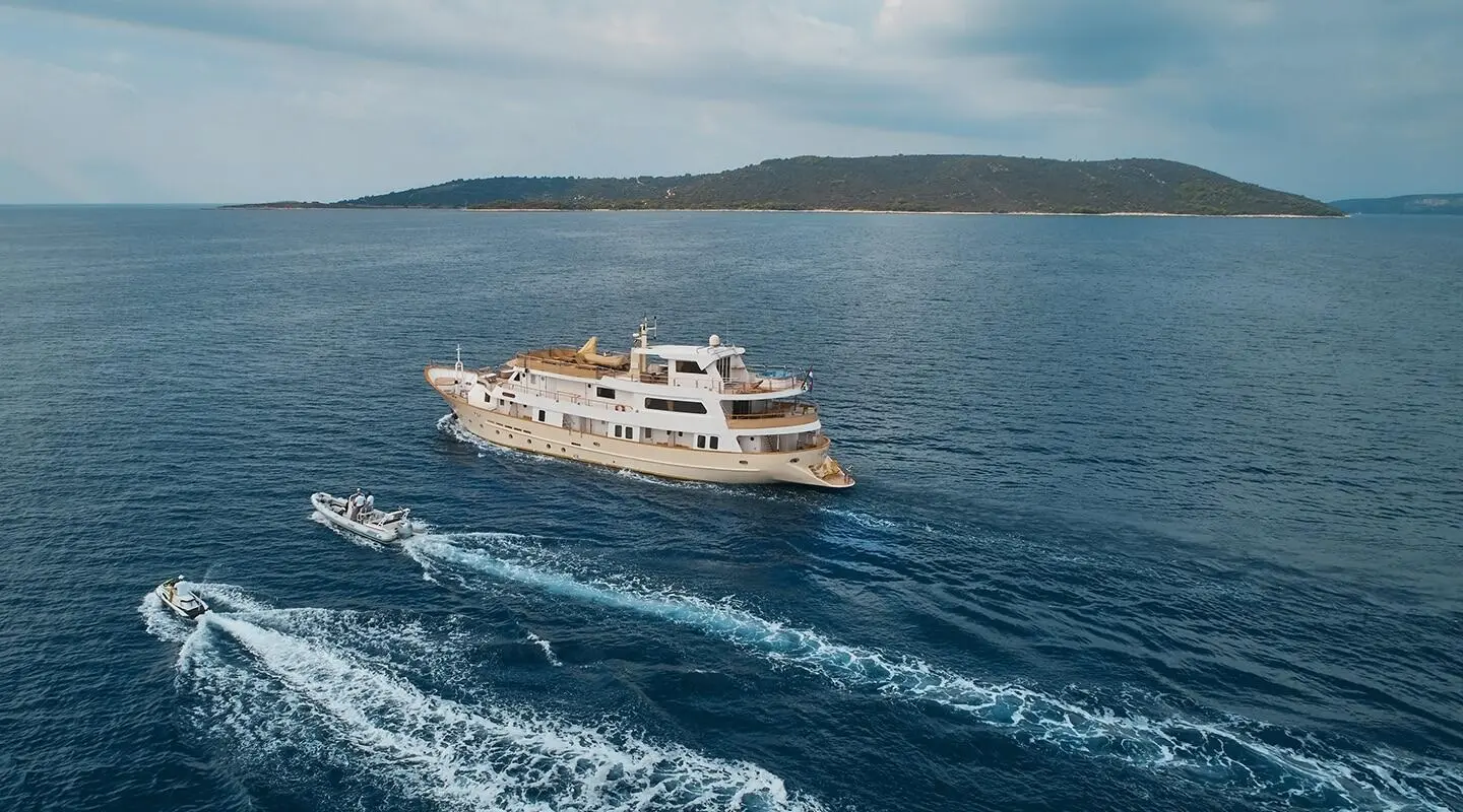 A large beige yacht on the sea with two motor speedboats nearby