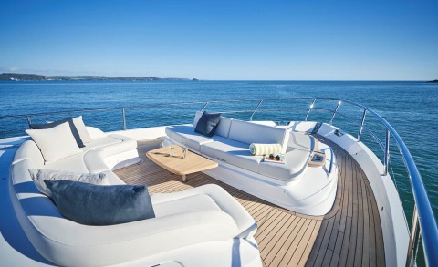 Luxurious yacht deck with white seating and a wooden table, blue sea and clear sky in the background