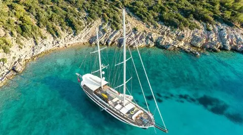 A white sailing yacht anchored in turquoise water near rocky shore at sunset