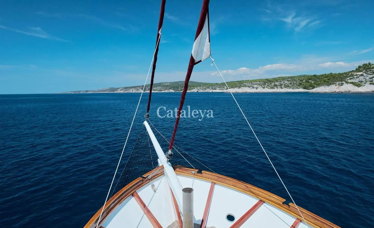 Bow of a yacht named Cataleya cutting through blue sea at sunset with rigging