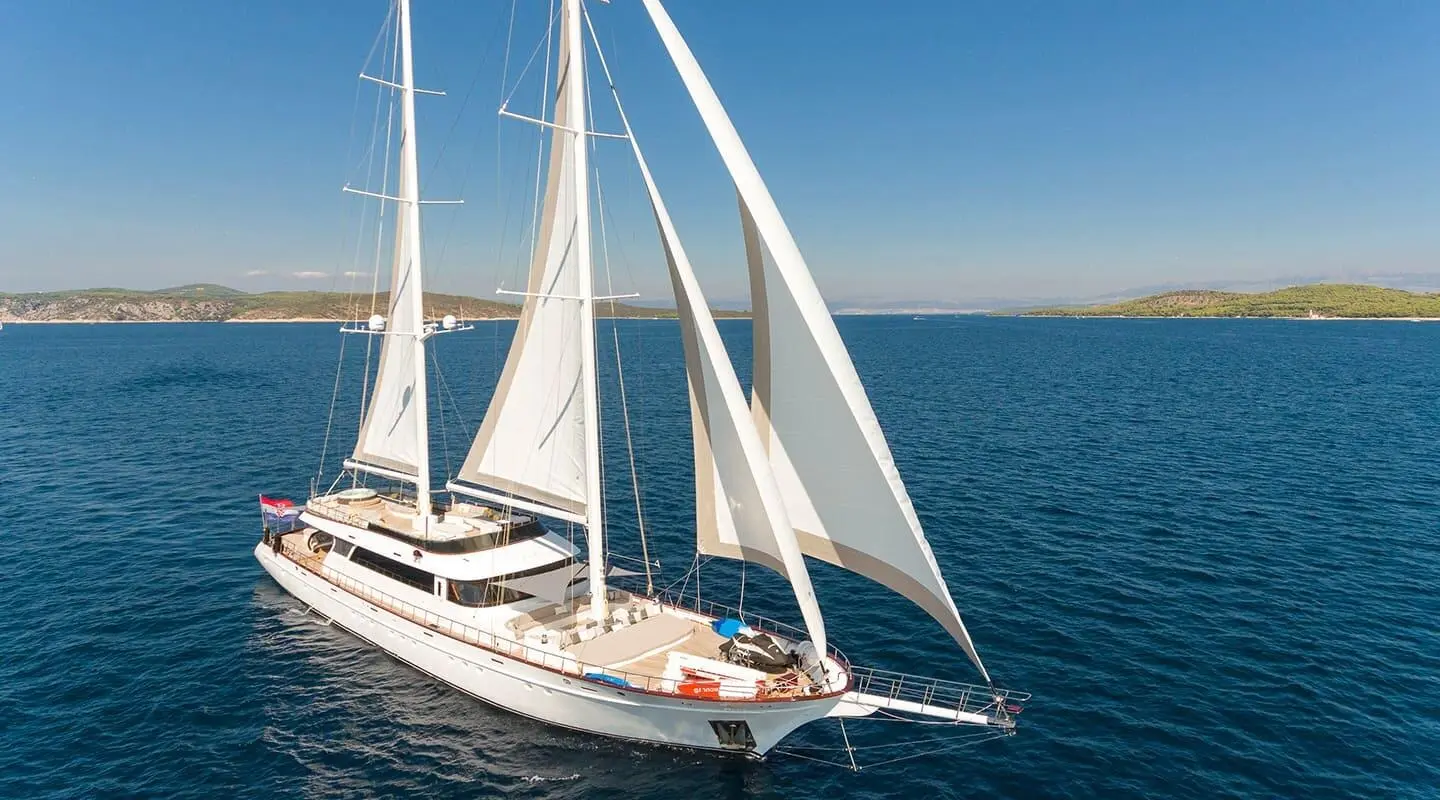 Lady Gita yacht with white sails anchored on calm blue sea at sunset