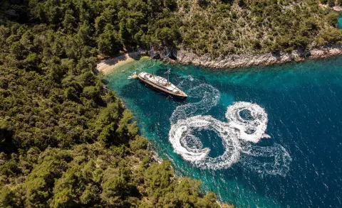 A luxury sailing yacht named Dalmatino anchored in clear blue water near rocky coastline