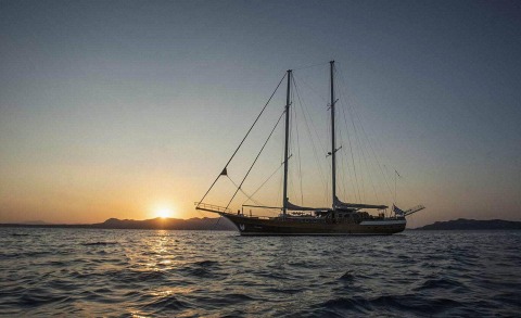 Sailing yacht Entre Cielos anchored on the sea at sunset with distant mountains on the horizon.