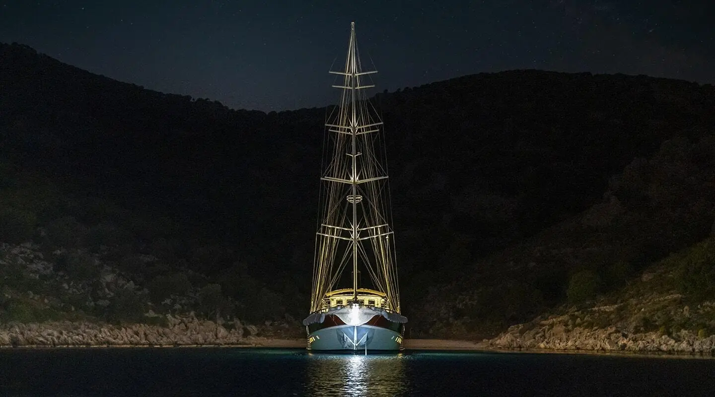 Gulet Tersane 8 at night, illuminated mast and sails, anchored in calm water