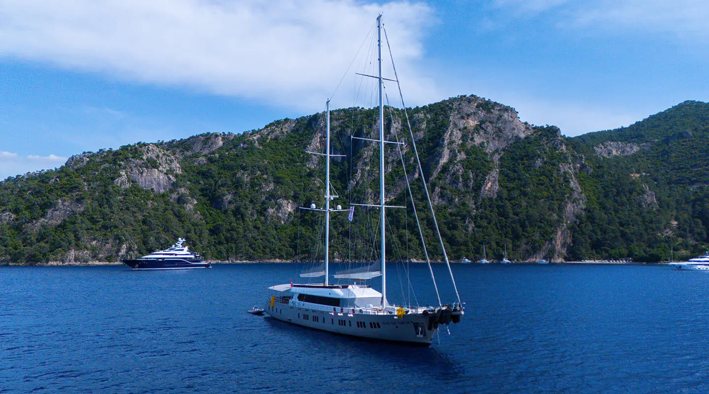 A large white sailing yacht anchored on calm blue water in a bay