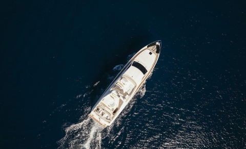 Overhead view of a white motor yacht named Lidia cruising in deep blue sea, visible open deck and seating area