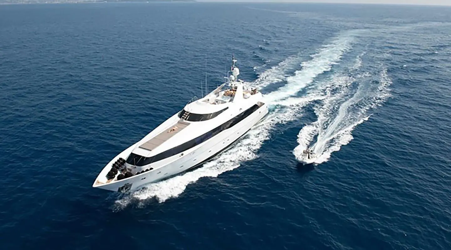 A sleek white yacht named Brooklyn speeds across blue sea, creating white wake