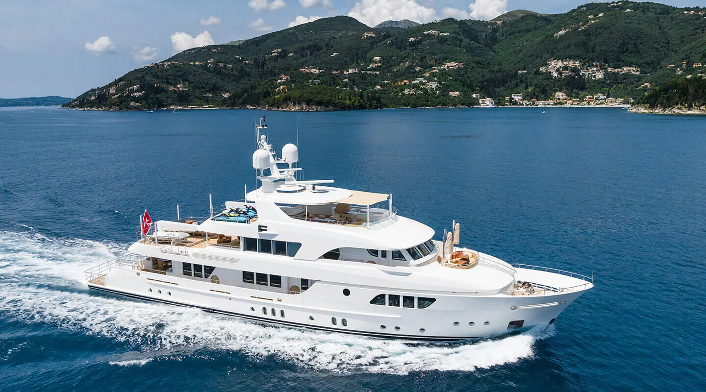 White motor yacht Serenity cruising on blue sea near green hills and coastline
