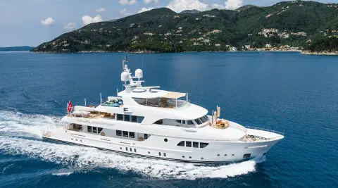 White motor yacht Serenity cruising on blue sea near green hills and coastline