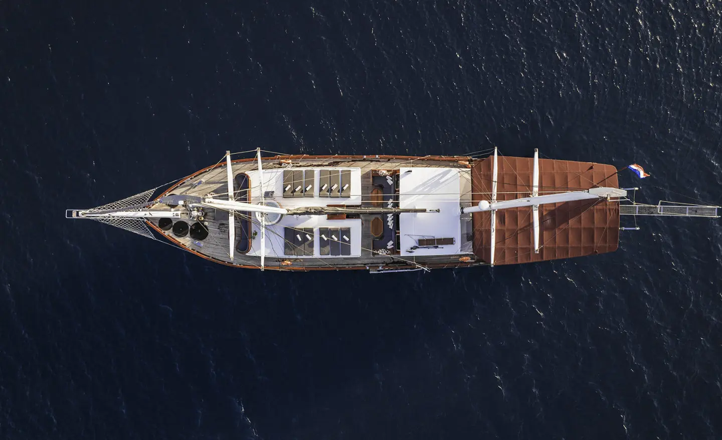 Aerial view of a white-and-brown gulet yacht sailing on calm deep blue sea