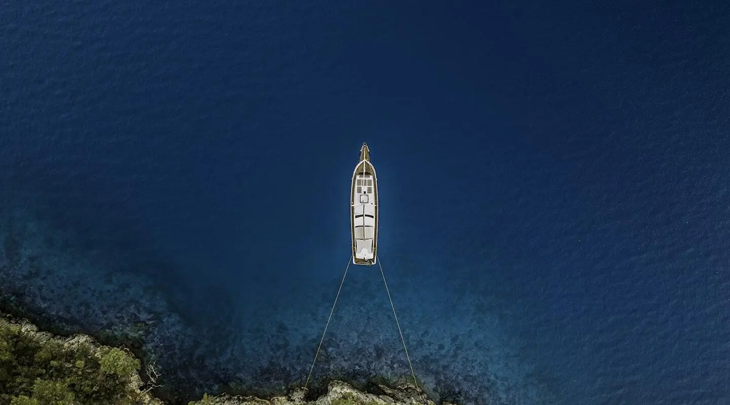 A sleek Belgin Sultan yacht anchored offshore, seen from above over deep blue sea