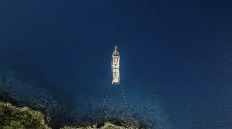 A sleek Belgin Sultan yacht anchored offshore, seen from above over deep blue sea