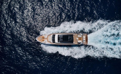 White and brown motor yacht cruising on dark blue sea, viewed from above