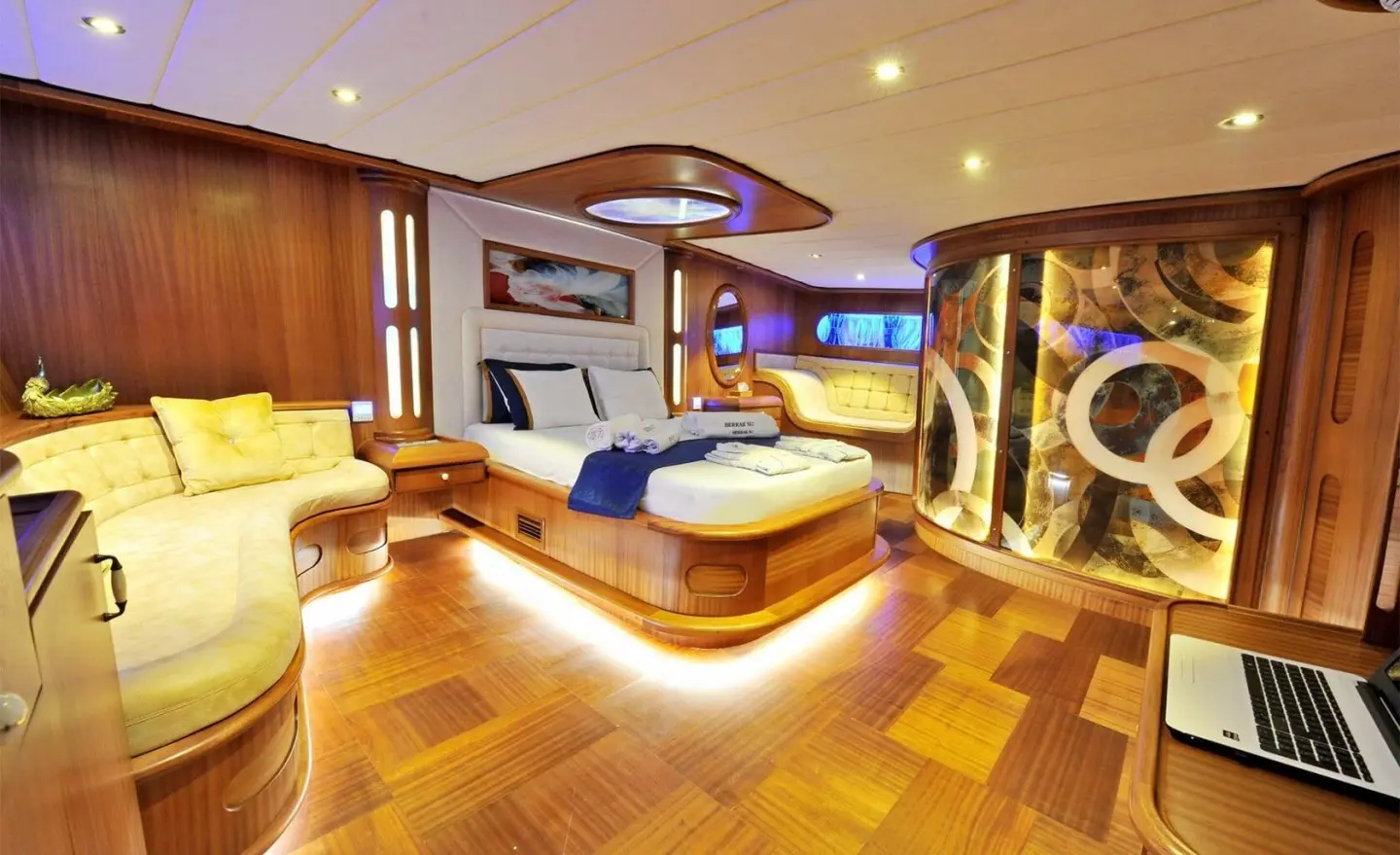 Interior of a yacht cabin with wooden panels, bed and sofa seating, modern lighting