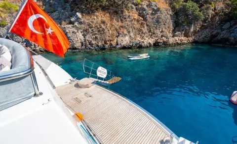 Esma Sultan yacht moored near rocky cliff, sunlit deck and clear blue sea