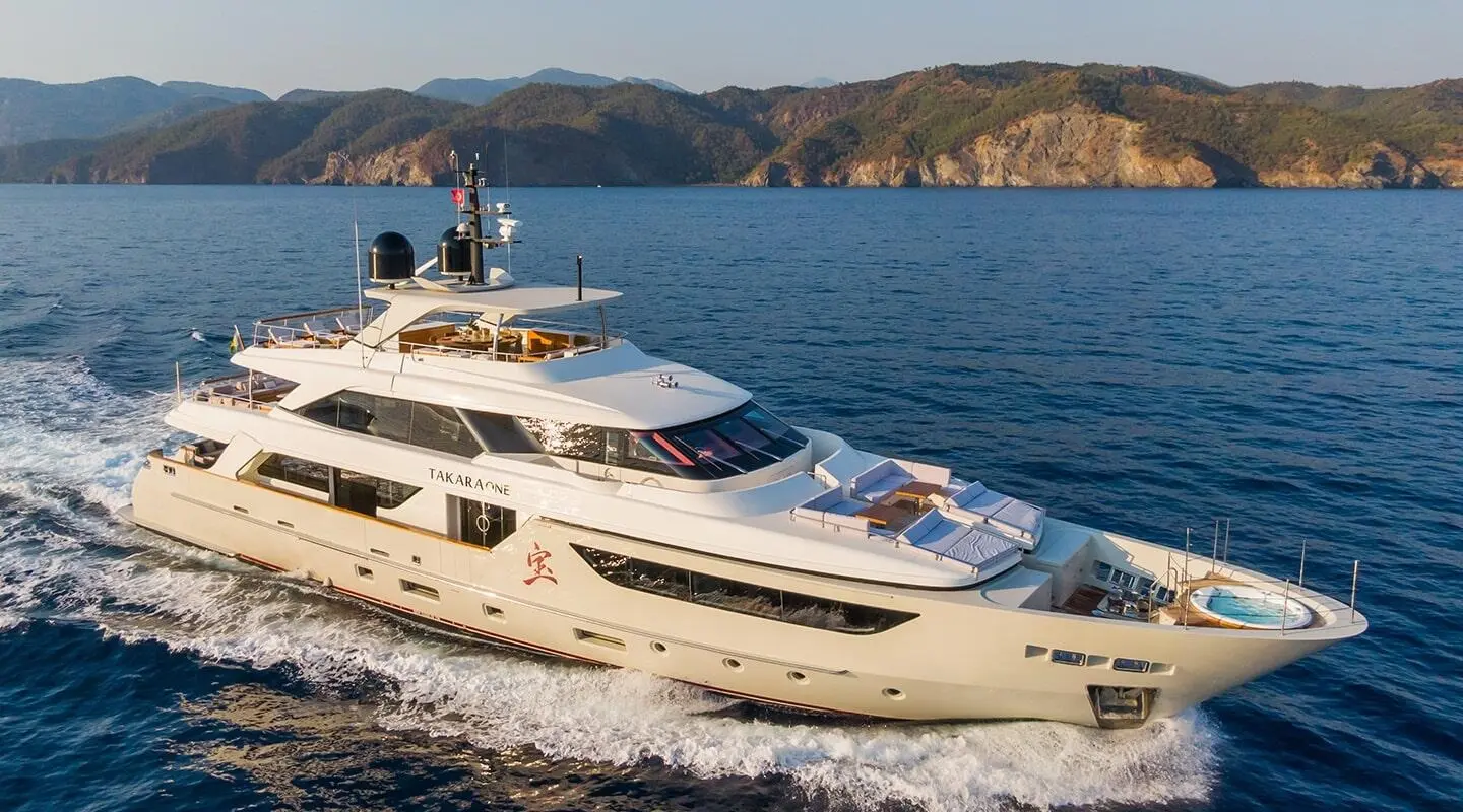 Takara One yacht cruising, white multi-deck motor yacht on blue sea with cliffs in background