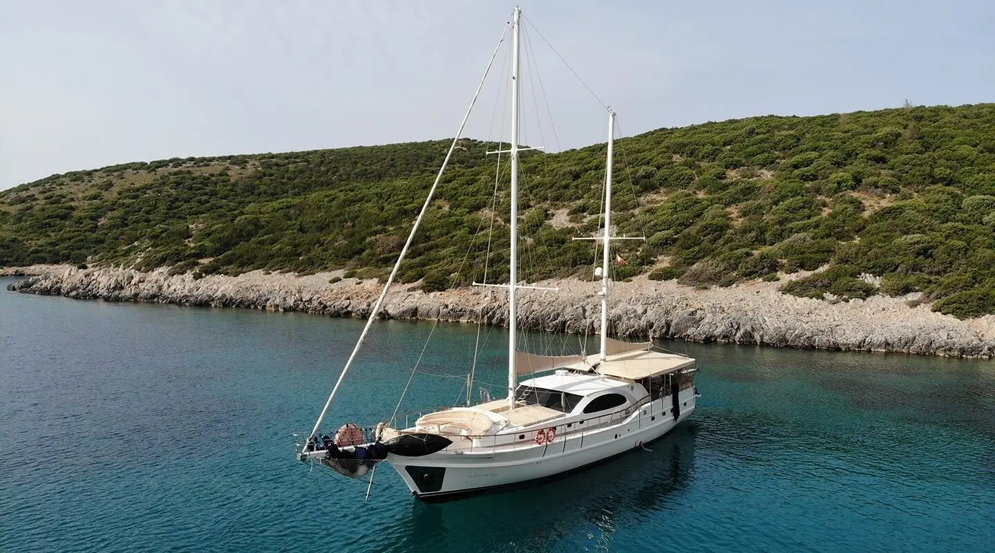 Queen Of Sea luxury sailing yacht anchored near rocky coastline with clear blue water
