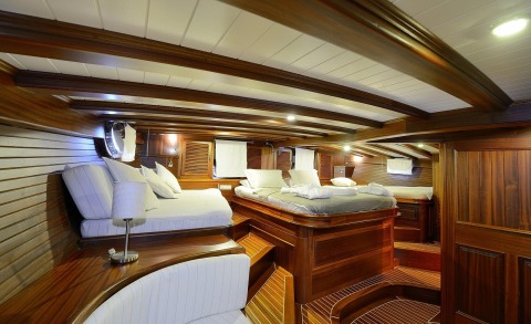 Wood-paneled interior of Zephyria II gulet with cushioned beds, steps, and small porthole windows visible