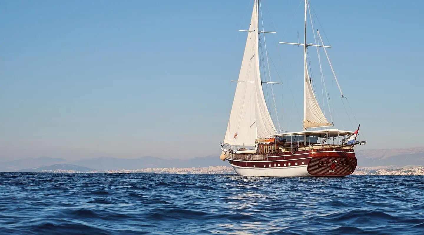Linda yacht anchored on calm blue sea at sunset with sails raised
