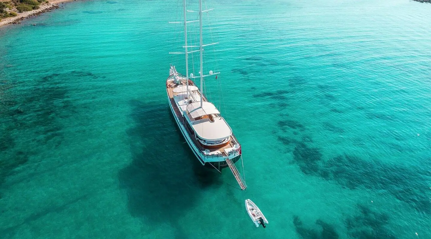 A sleek yacht anchored in turquoise calm waters at dusk with a small boat nearby