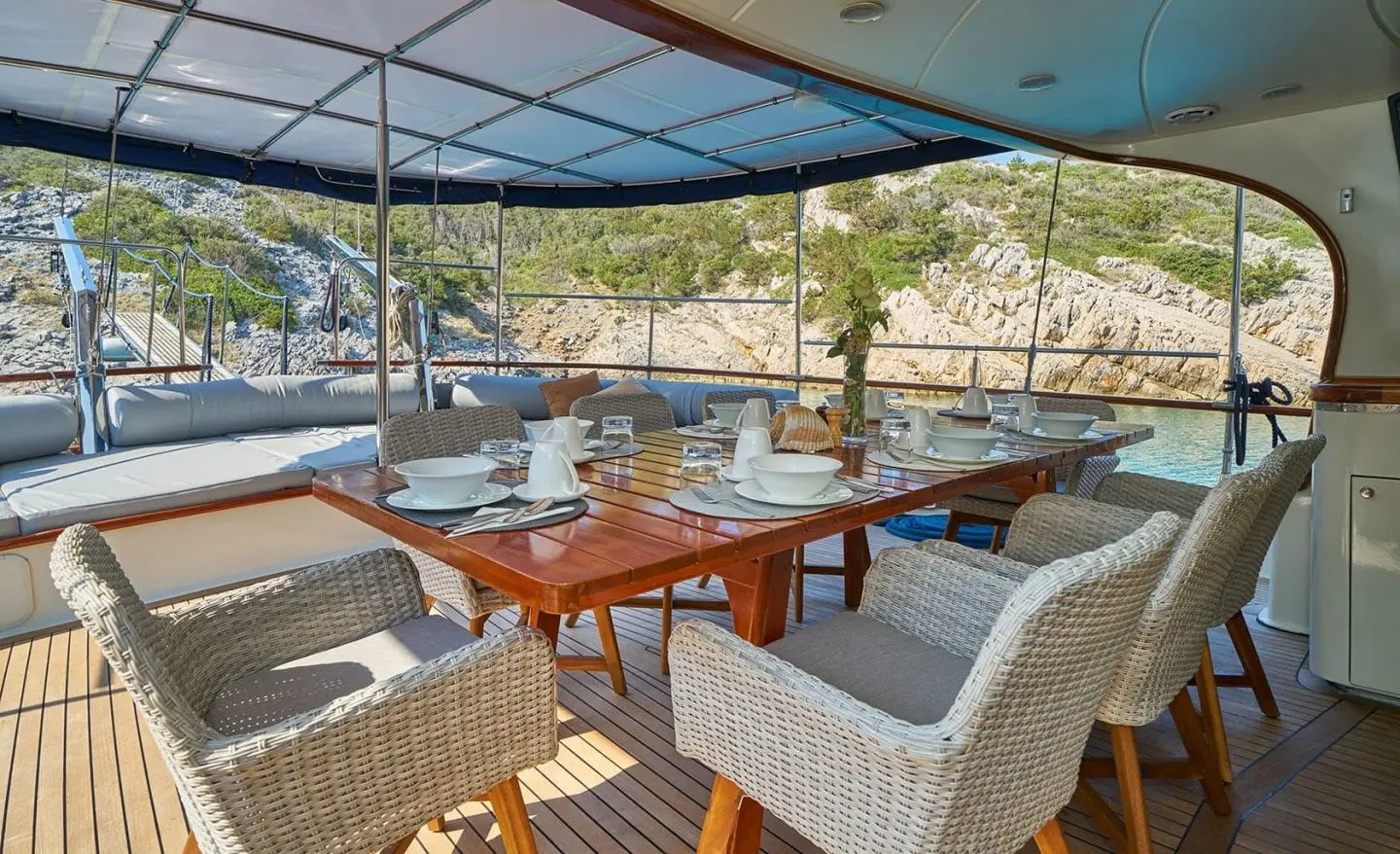 Lotus yacht dining area on deck with wooden table, cushioned chairs, sunset harbor view
