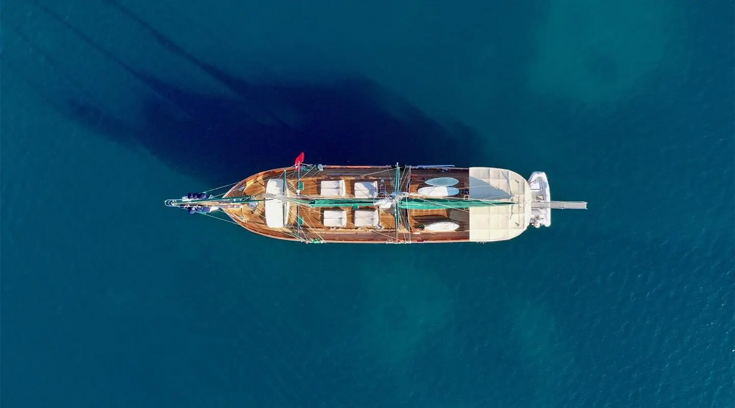 Top-down view of Ros Mare yacht anchored on calm turquoise sea at sunset