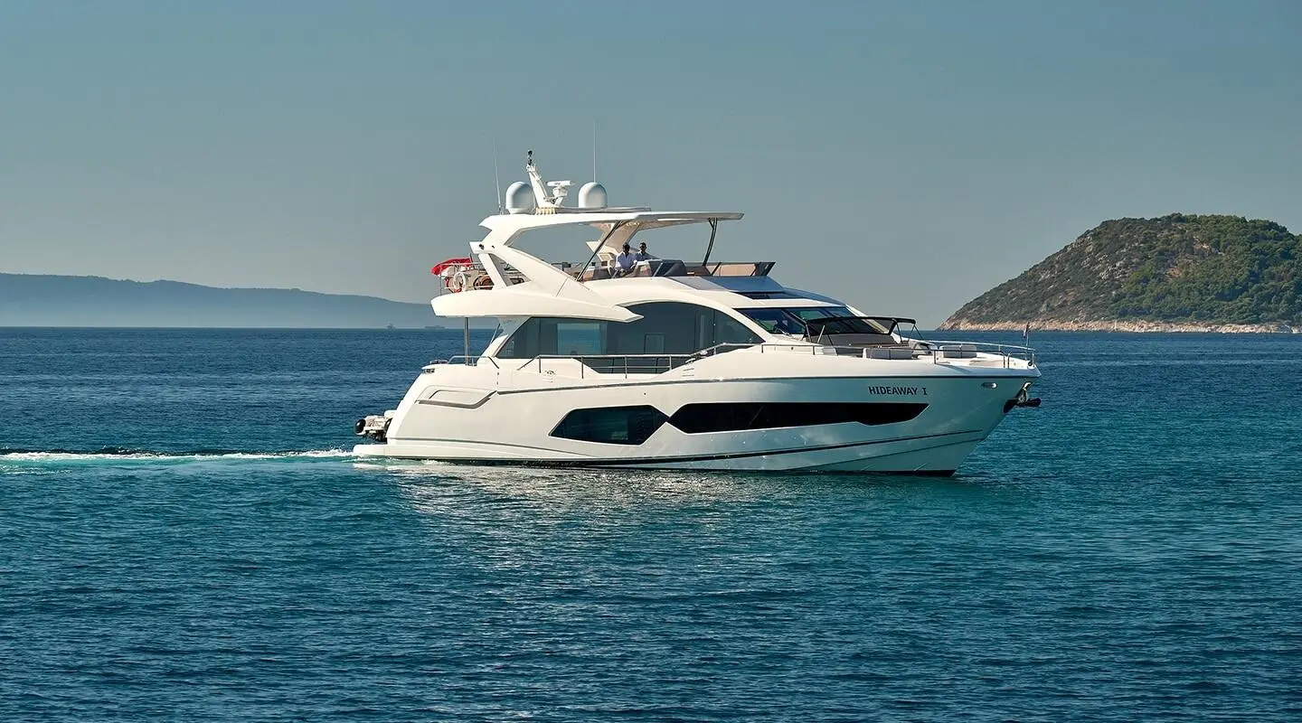 White luxury yacht Hideaway I glides on calm blue waters near a rocky coastline