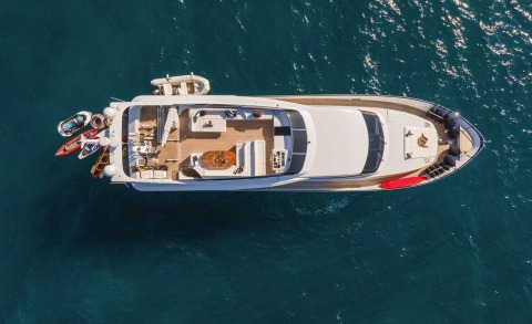 White motor yacht viewed from above with open deck and sunlit seating, water and water toys along the side