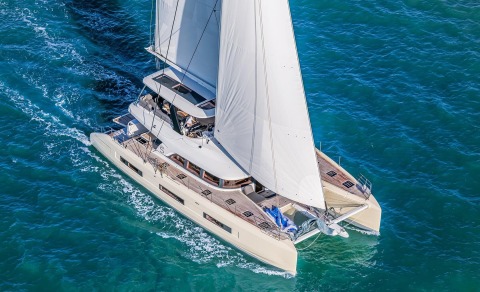 Top-down view of a white sailing yacht with blue sea background and wooden deck