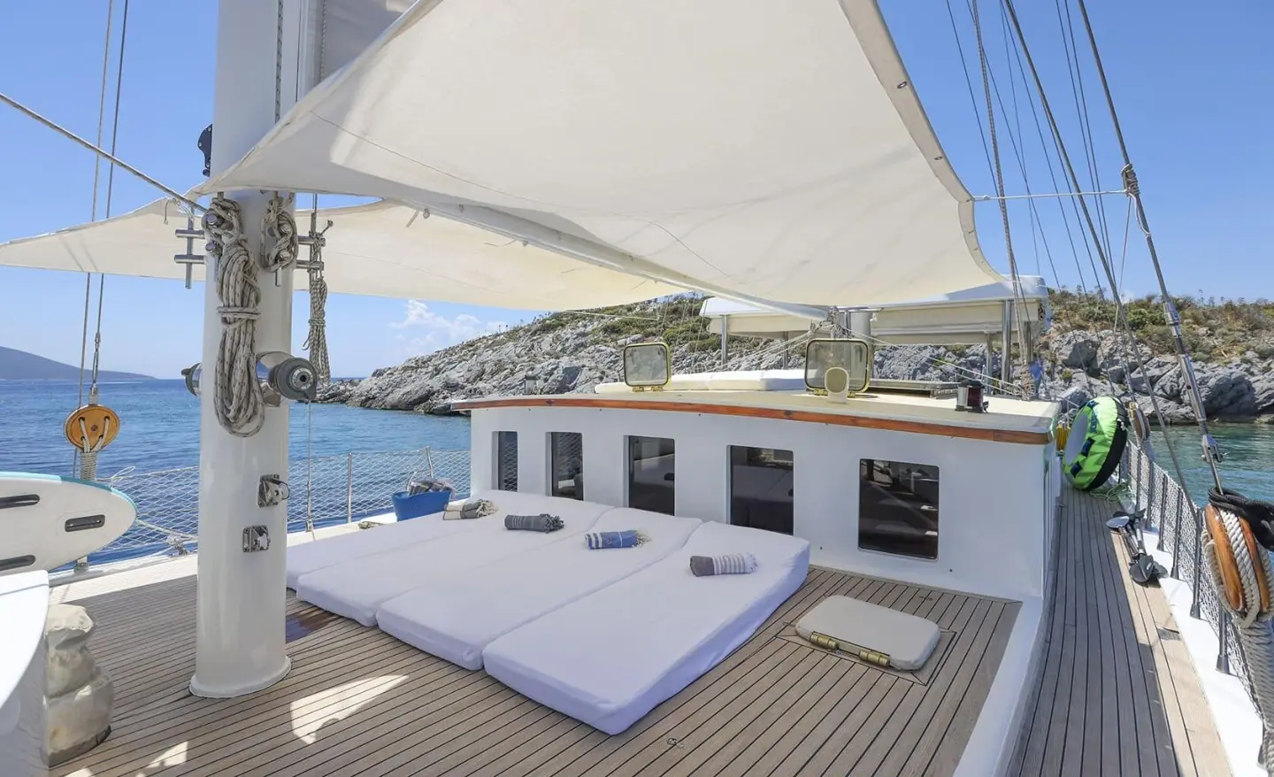 Gazella yacht deck with seating area, blue cushions, sails and ocean view at sunset