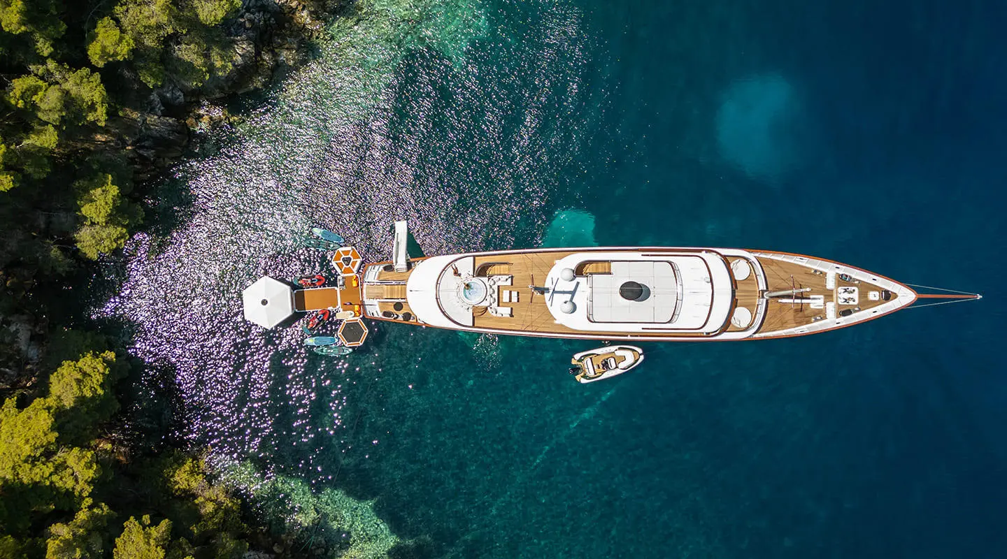 Top-down view of Maia yacht anchored along rocky shoreline with clear blue water