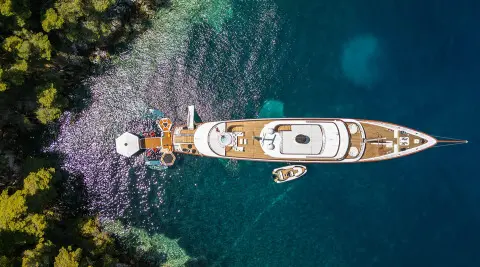 Top-down view of Maia yacht anchored along rocky shoreline with clear blue water